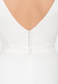 Rückseite eines weißen Kleides mit tiefem V-Ausschnitt, ausgestattet mit einem versteckten Reißverschluss und sechs mit Stoff bezogenen Knöpfen entlang der Wirbelsäule.