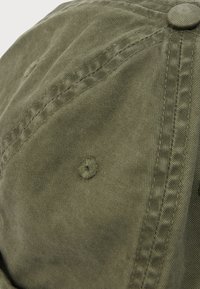 Κοντινό πλάνο ελαιώδους πρασινού υφάσματος με ραφές και κουμπί καλυμμένο με ύφασμα, που δείχνει λεπτομερείς υφές και ραφές.