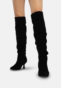 Zwarte over-de-knie laarzen van zacht suède met een nonchalant ontwerp, puntige neus en stilettohak; voorzien van een ritssluiting aan de zijkant.