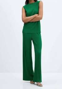 Ensemble deux pièces vert à côtes comprenant un top sans manches et un pantalon à jambes larges. Tissu texturé, finition lisse, associé à des talons avec lanières.