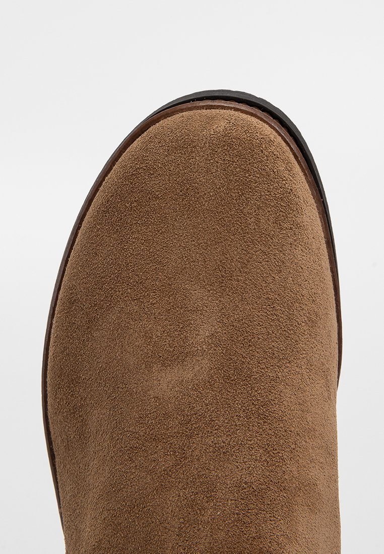 Brauner Wildlederstiefel mit schwarzer Gummisohle, von oben vor einem schlichten hellen Hintergrund gezeigt.