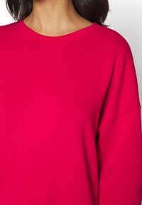 Fuchsia sweatshirt met een ronde halslijn en lange, losse mouwen. Zacht, glad materiaal met minimale stikseldetails.