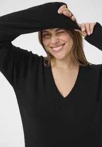 Schwarzer Strickpullover mit V-Ausschnitt, langen Ärmeln und gerippten Bündchen, der eine weiche Textur und einen lässigen Schnitt aufweist.