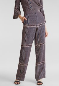 Mönstrad jumpsuit i marinblått med geometriska mönster i rött och vitt. Har vida ärmar, figursydd midja och lösa, raka ben.