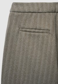 Braunes Stoff mit Fischgrätenmuster und strukturierter Oberfläche. Verfügt über eine einzelne Gesäßtasche mit sauberer Kante und dezentem Nahtdetail.