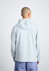 Ljusblå fleece-hoodie med avslappnad passform, som har en stor huva och en mjuk textur. Enkel design utan mönster eller synlig hårdvara.