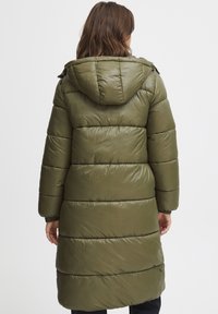 Oliven grønn puffjakke med hette, som har en quiltet design, lange ermer og ribbestrikkede mansjetter, som rekker midt på leggen med en glatt finish.