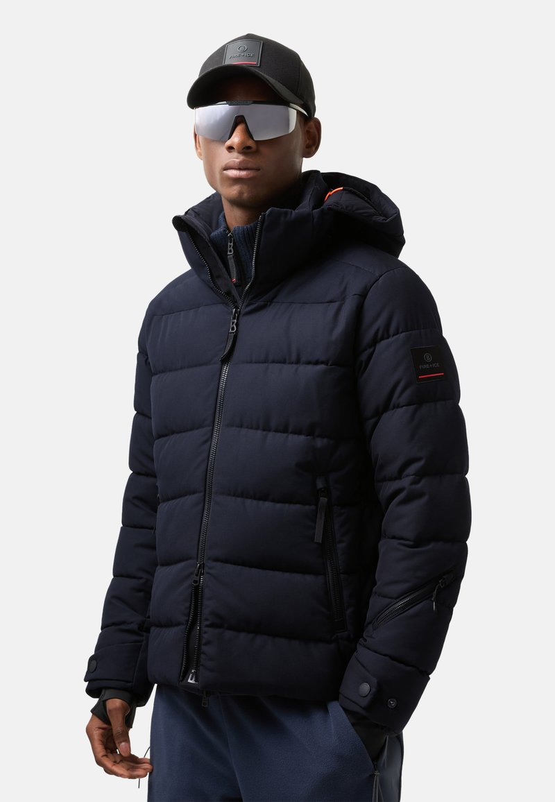 Námořnická puffer bunda se zapínáním na zip, elastickými manžetami a dvěma bočními kapsami na zip. Obsahuje kapuci a nášivku s logem na rukávu.