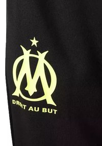 Tessuto nero con un grande logo giallo con la lettera "M" e una stella sopra, accompagnato dal testo "DROIT AU BUT" sotto.