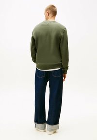 Felpa verde oliva con colletto a girocollo, polsini e orlo a costine. Abbinata a jeans in denim blu scuro dal fit morbido con orli arrotolati.