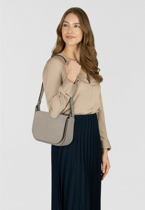 Graue Leder-Schultertasche mit glatter Textur und Klappverschluss, getragen von einer Person in beige Bluse und dunklem Faltenrock.