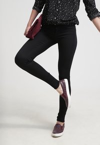 Černé přiléhavé kalhoty v kombinaci s černobílou košilí se vzorem hvězd. Burgundské slip-on boty a odpovídající psaníčko doplňují outfit.