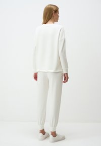 Felpa bianca e pantaloni joggers in materiale morbido, con polsini elastici e vestibilità comoda, indossati con sneaker bianche, visti da dietro.