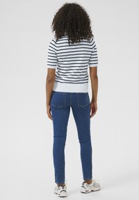 Triibuline lühikeste varrukatega kampsun valget ja tumesinist värvi, koos siniste kitsaste teksadega. Mudel kannab valgeid tossusid. Vaade tagant.