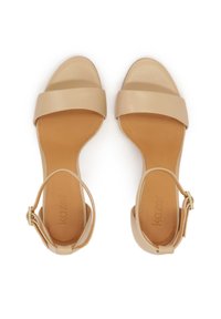 Beige leather sandals with wide front straps, ankle buckle, and a smooth finish. They feature a flat sole and a simple, elegant design.