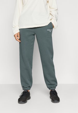 Dark green sweatpants with elastic cuffs, featuring a subtle white logo on the thigh. Paired with a light long-sleeve top and black sneakers.