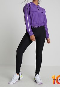Purple cropped windbreaker with white stripes, black ribbed leggings, and white sneakers with purple accents and branded straps.