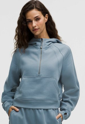 Sweat-shirt court bleu clair en tissu doux. Comprend une fermeture éclair à l'avant, une capuche et une poche avant, avec des poignets et un ourlet côtelés.