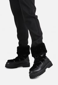 Botas negras con un puño de piel sintética, que cuentan con una suela gruesa y un diseño con cordones. La parte superior es una mezcla de cuero suave y tela texturizada.