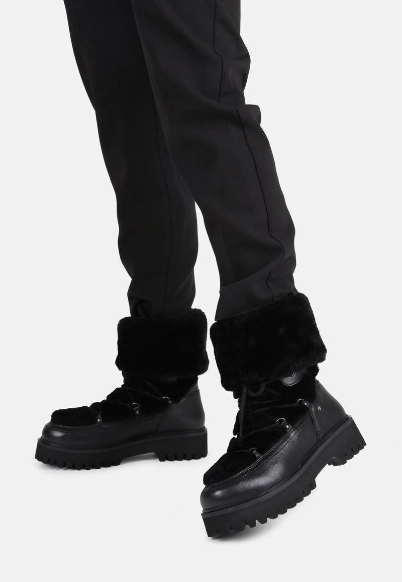 Botas negras con un puño de piel sintética, que cuentan con una suela gruesa y un diseño con cordones. La parte superior es una mezcla de cuero suave y tela texturizada.