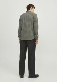 Chemise à manches longues noire à motifs avec un col boutonné, vue de dos, associée à un pantalon foncé et des chaussures noires.