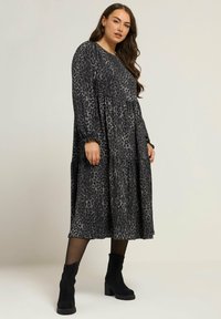Czarna i szara sukienka w panterkę z długimi rękawami, warstwowym krojem i okrągłym dekoltem. Stylizowana z czarnymi botkami za kostkę.