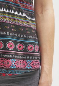 Camiseta sin mangas con estampado que presenta una base negra con diseños geométricos y florales multicolores en rosa, azul, amarillo y blanco. Tejido suave.