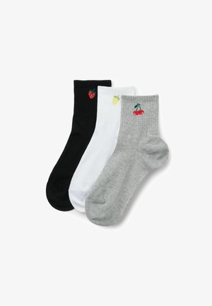Trois chaussettes courtes aux chevilles en noir, blanc et gris, chacune ornée d'une petite broderie de fruit : fraise, citron et cerise, respectivement.