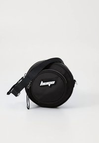 Kerek fekete nejlon táska texturált felülettel, két cipzáras rekesszel, állítható pánttal és feltűnő fehér logóval.