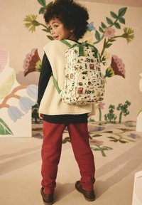 Batoh s krémovou tkaninou, zdobený barevnými a hravými vzory kaktusů, zvířat a přírody. Zelené popruhy a detaily; obdélníkový tvar.