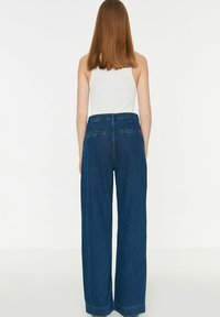 Pantaloni in denim blu a gamba larga con vita alta, caratterizzati da un design classico e tasche posteriori. Texture liscia con una finitura pulita.