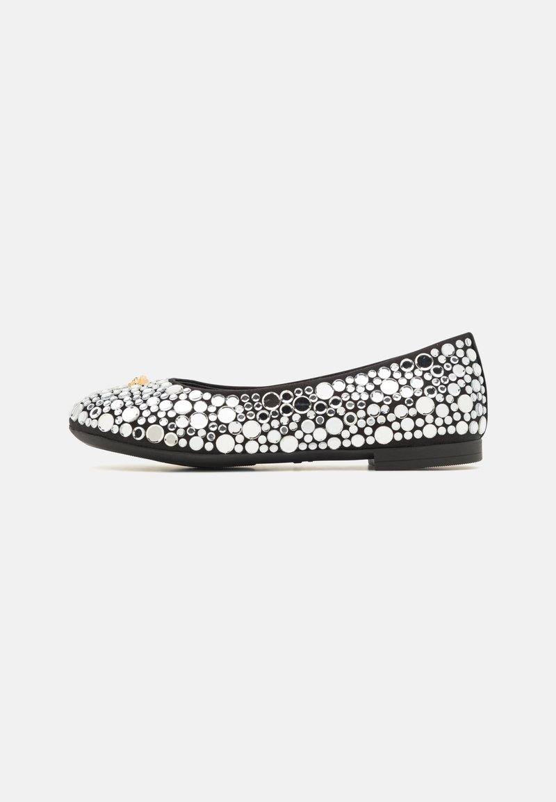 Mocasin negro de ballet con punta redondeada, adornado con un patrón de tachuelas circulares en plata y blanco, y una suela plana y flexible.