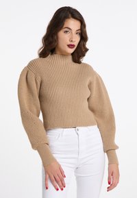 Maglione beige a coste con collo alto e maniche voluminose, abbinato a jeans bianchi aderenti con un tessuto testurizzato.