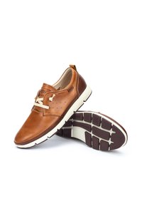 Brązowe casualowe buty ze skóry z białymi gumowymi podeszwami, beżowymi sznurowadłami i perforowanymi detalami po bokach, prezentowane na białym tle.