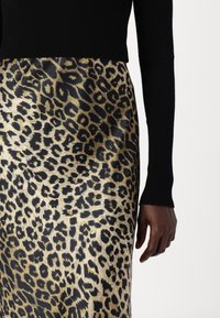 Black ribbed long-sleeve top paired with a leopard print midi skirt in gold and black, featuring a smooth texture and bold animal pattern.