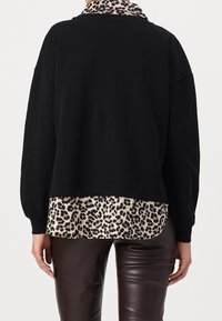 Felpa nera oversize con un strato inferiore a stampa leopardo. Tessuto morbido, maniche lunghe, orlo arrotondato e colletto con un motivo contrastante.