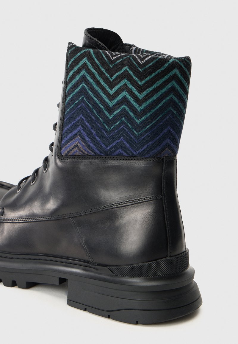 Sorte læder ankelstøvle med en mønstret overdel i blå og grøn stof. Har en robust sål og teksturerede detaljer.