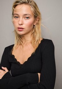 Sort ribbet top med en bølget blondeudskæring og lange ærmer, der har en tætsiddende pasform. Stoffet ser blødt ud med en let tekstur.