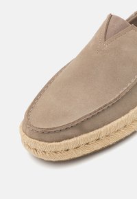 Brune ruskinds slip-on sko med rund tå og en vævet jute sål for tekstur og holdbarhed. Minimal syning fremhæver designet.