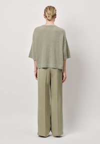 Lichtgroene, losgebreide trui met brede mouwen, gecombineerd met hoogwaist, lichtgroene, wijde broek van soepel materiaal.