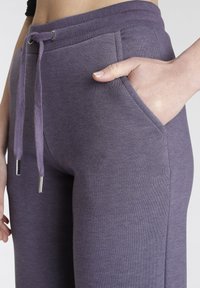 Paarse joggingbroek met een trekkoord in de taille, zijzakken en ribbelboorden. Gemaakt van zachte stof met een gladde textuur.