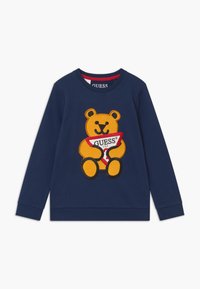 Felpa blu navy con una grande grafica di un orsetto giallo che tiene un'etichetta triangolare rossa e bianca con il testo "GUESS". Tessuto misto cotone.