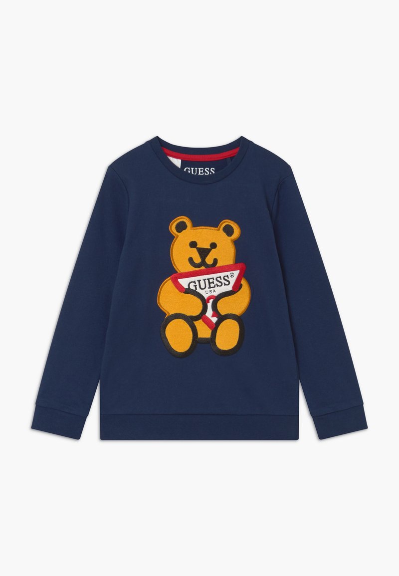Felpa blu navy con una grande grafica di un orsetto giallo che tiene un'etichetta triangolare rossa e bianca con il testo "GUESS". Tessuto misto cotone.