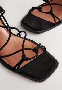 Sandali neri con punta quadrata in morbido camoscio, dettagliati con sottili cinturini neri annodati e una soletta beige.