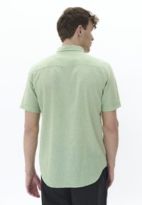 Camicia a maniche corte di colore verde chiaro con tessuto leggermente testurizzato, colletto button-down e orlo arrotondato. La vista posteriore mostra i dettagli delle cuciture.