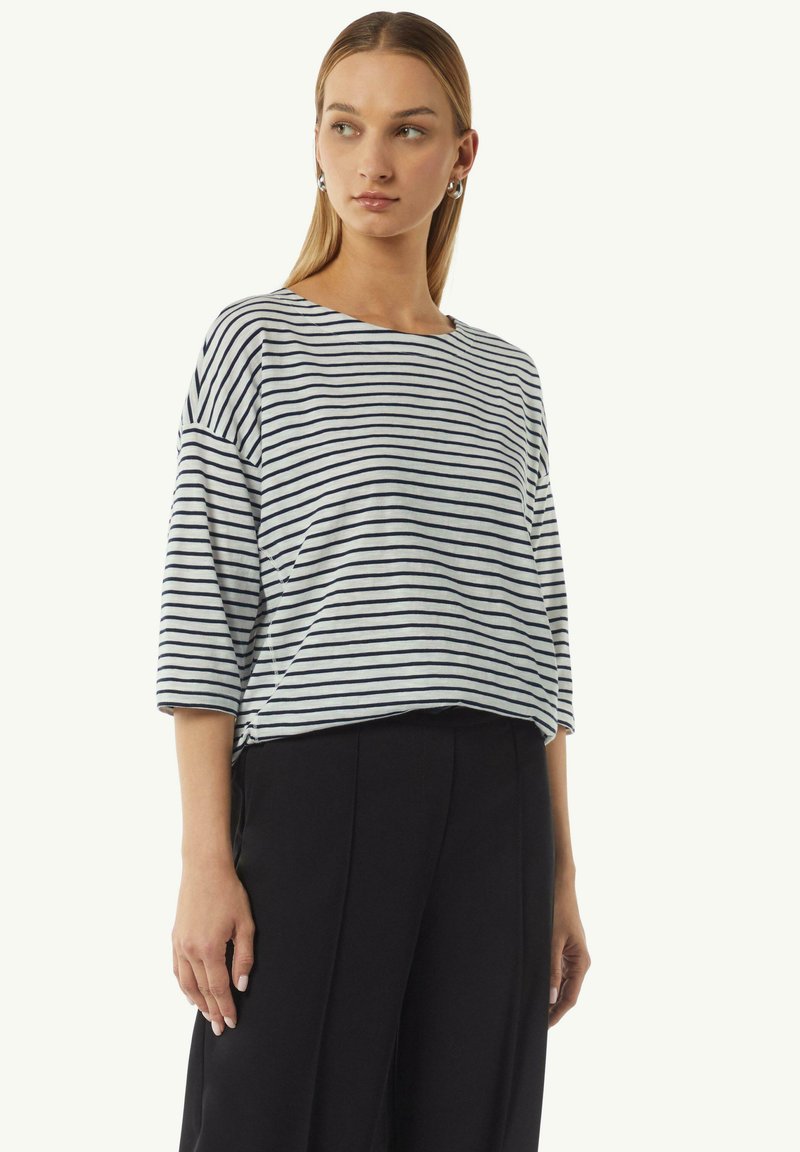 Gestreepte lichtgewicht top in lichtgrijs en marineblauw; losse pasvorm, wijde mouwen en een ronde halsuitsnijding. Gecombineerd met zwarte geplooide broek.