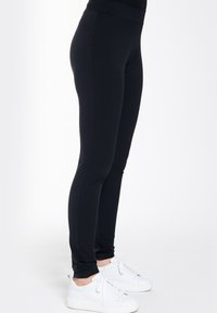 Zwarte leggings van rekbaar materiaal. Hoge tailleband, aansluitend ontwerp en een gladde textuur. Gecombineerd met witte sneakers.