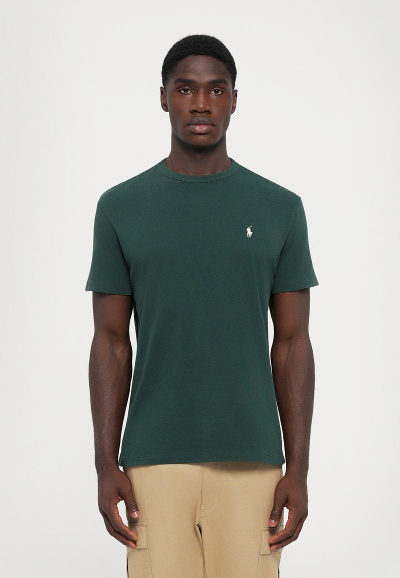 T-shirt en coton vert avec un col rond, des manches courtes et un petit logo brodé blanc sur la poitrine gauche. Texture lisse.