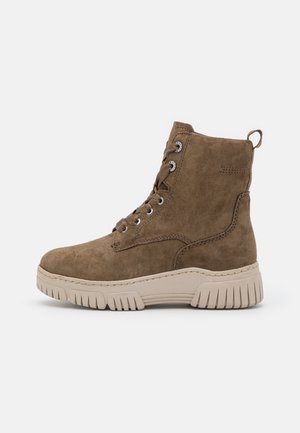 Brown suede ankle boot with lace-up design, silver eyelets, and a chunky beige rubber sole featuring prominent ridges.
