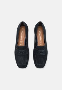 Mocassins en daim bleu foncé avec une semelle plate, présentant un détail cousu et un rabat décoratif sur le dessus. Taille 37.